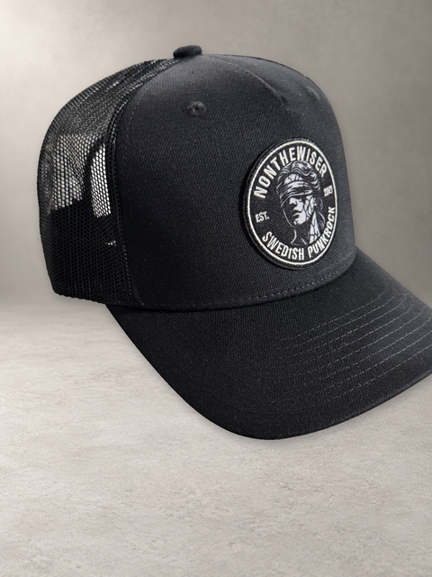 Nonthewiser Trucker High, svart keps på grå stenyta, från sidan